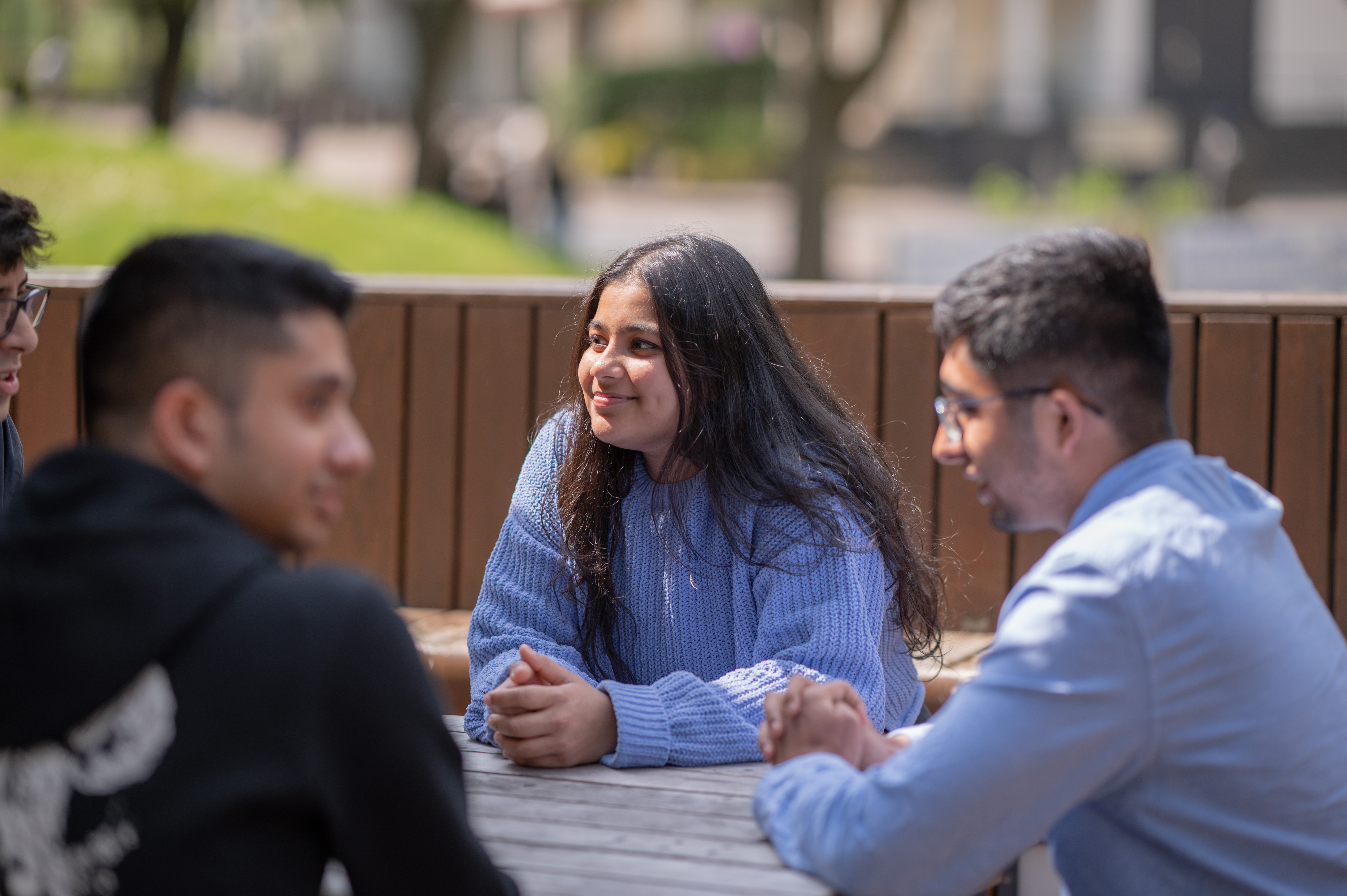 Three students sit around a table discussing Philosophy. They are outside the faculty of Arts Building.