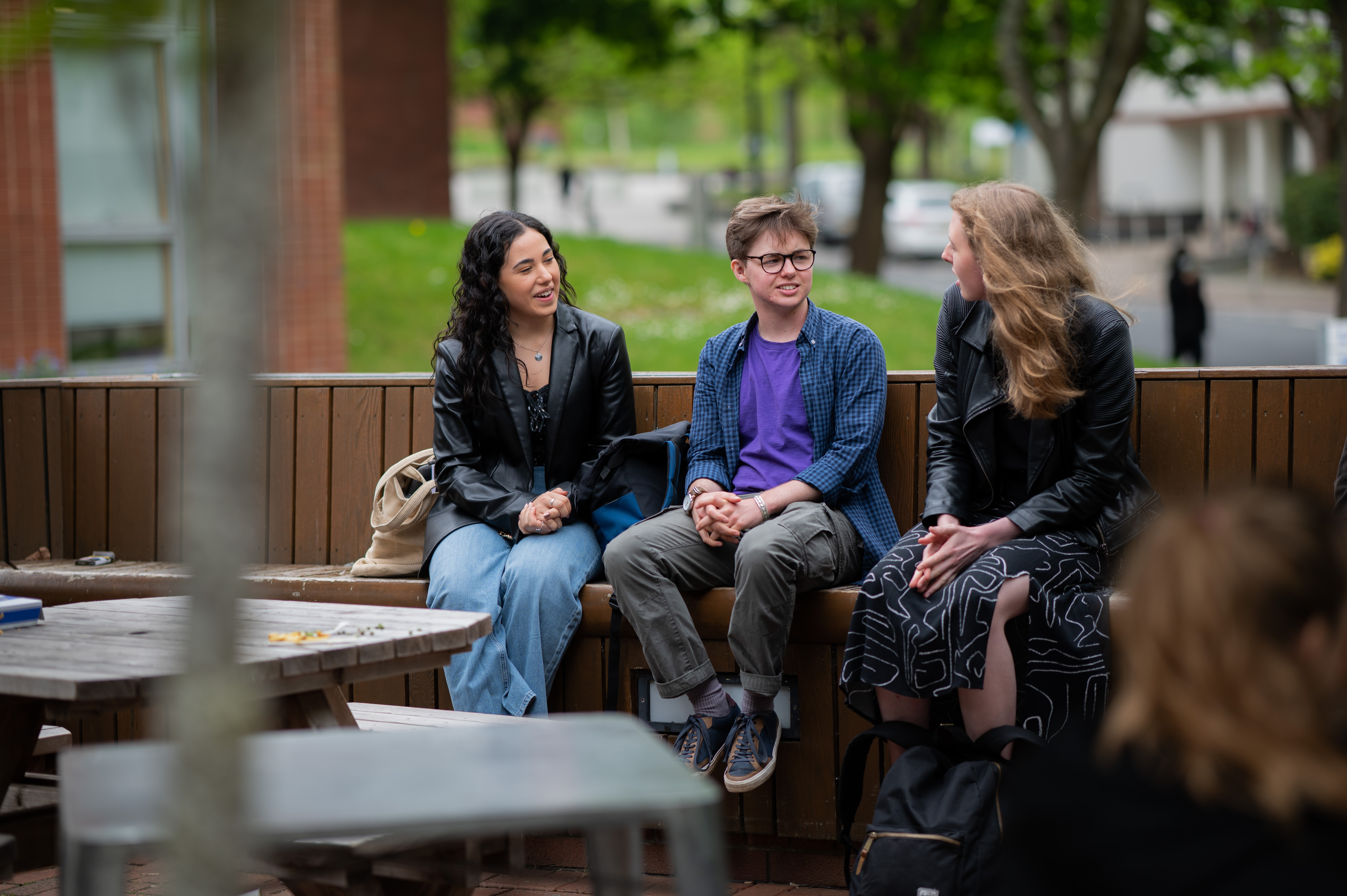 Three students are sat outside the Faculty of arts building having an engaging discussion. There are trees in the background