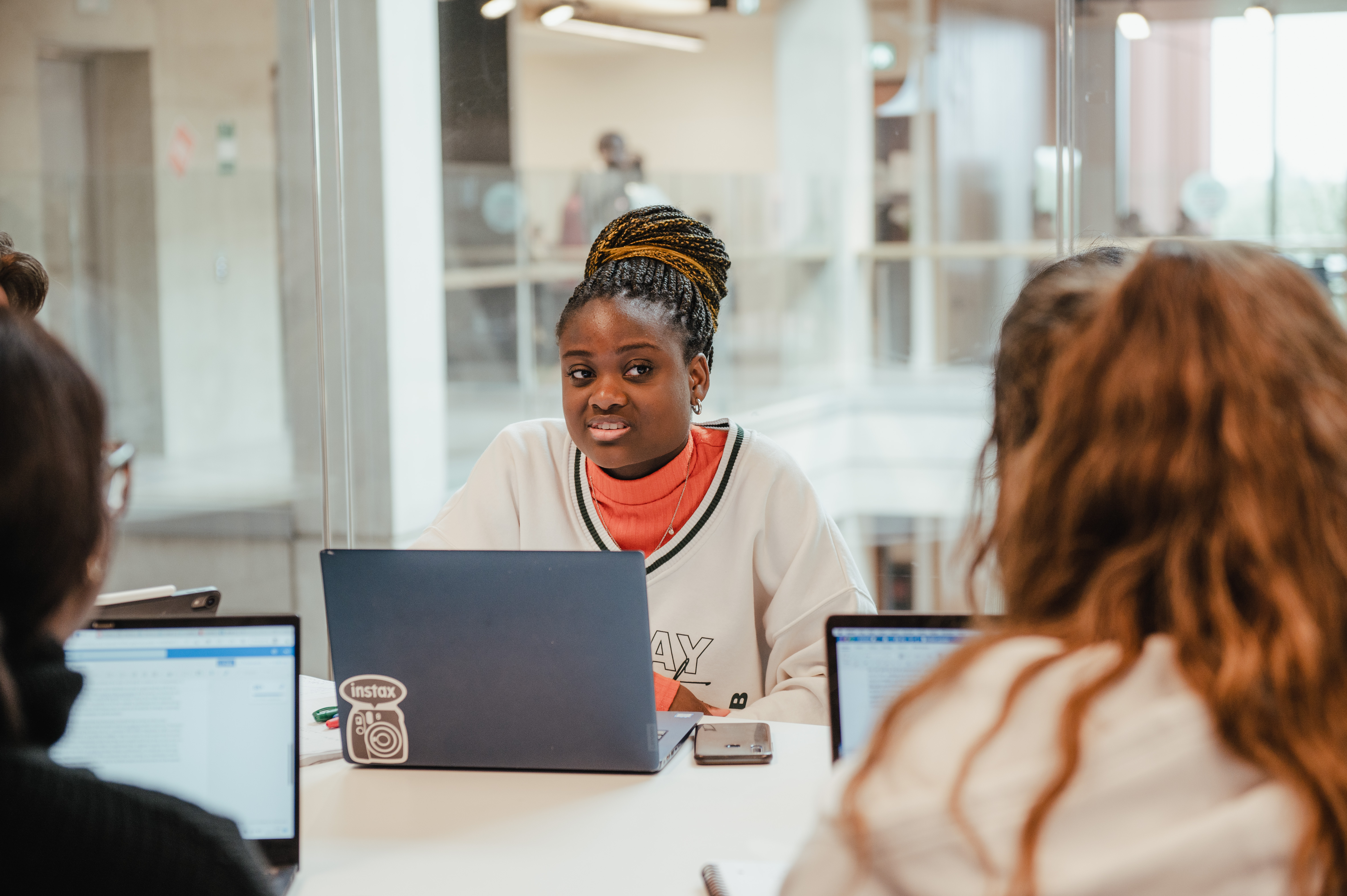 Three students are working at their laptops. two are facing away from us and the third is facing us and smiling