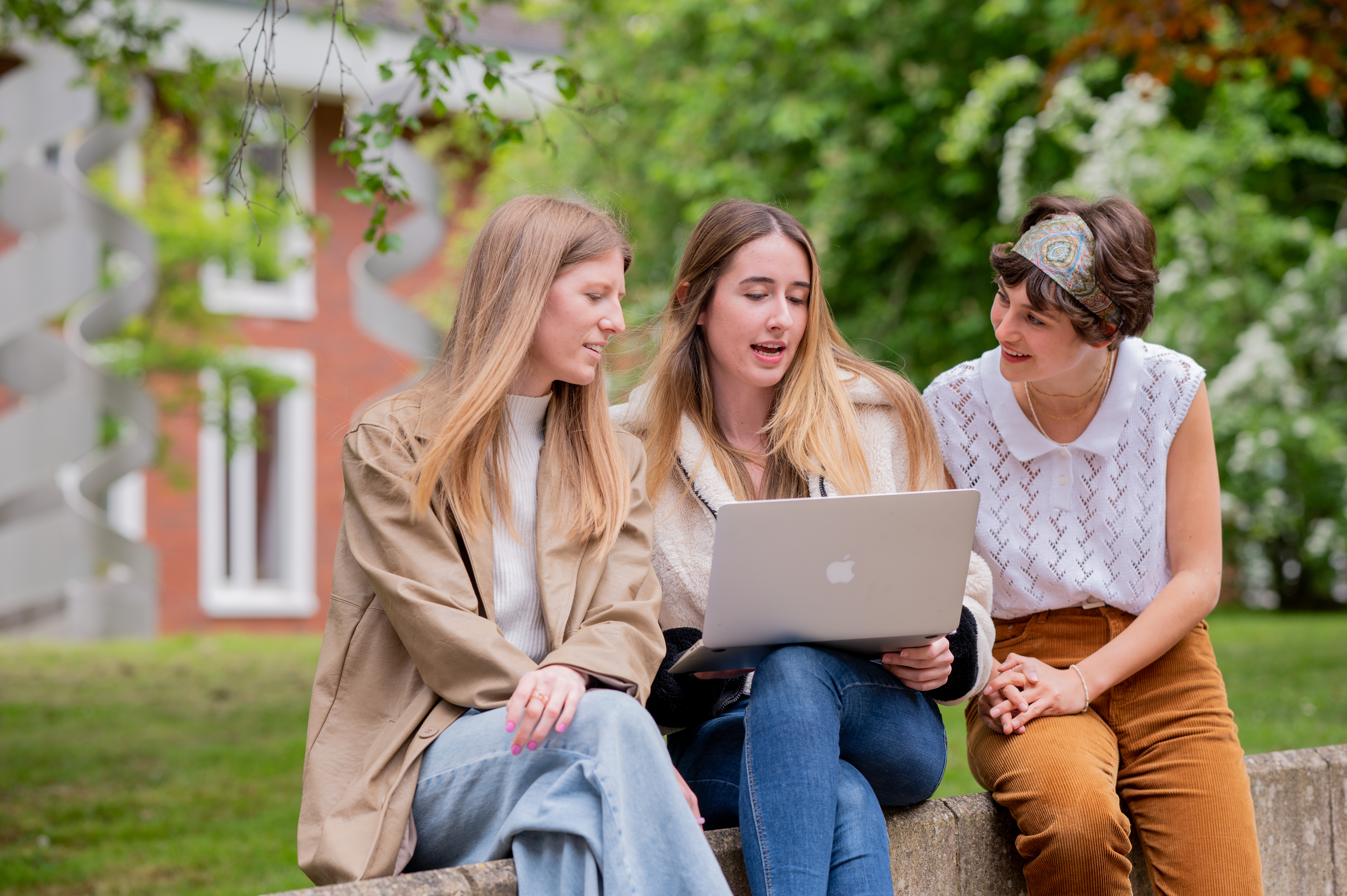 A group of three Philosophy students sit on a bench looking at a laptop