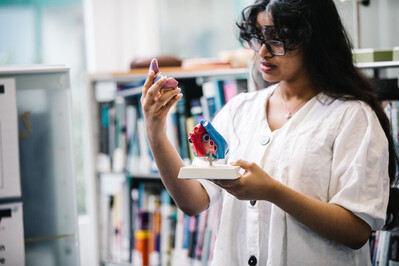 A female student in a lab setting, gesturing towards a sample in her hand