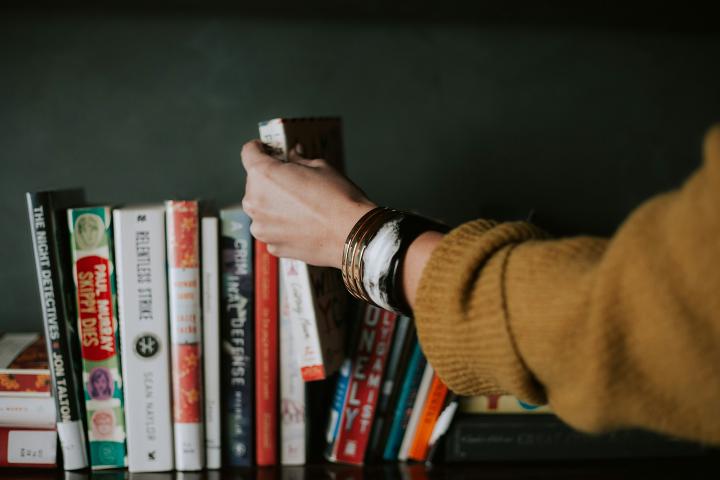 A hand reaches out to remove a book from a row of books along a shelf