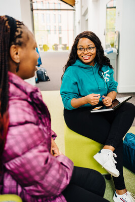 Two students, sat side by side, smiling at each other.