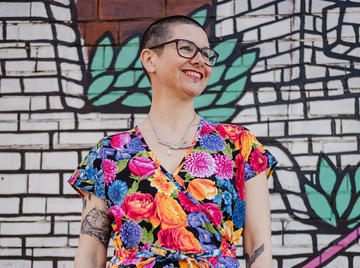 Bea Marshall headshot - Bea wears a bright flowery dress against a graffiti wall