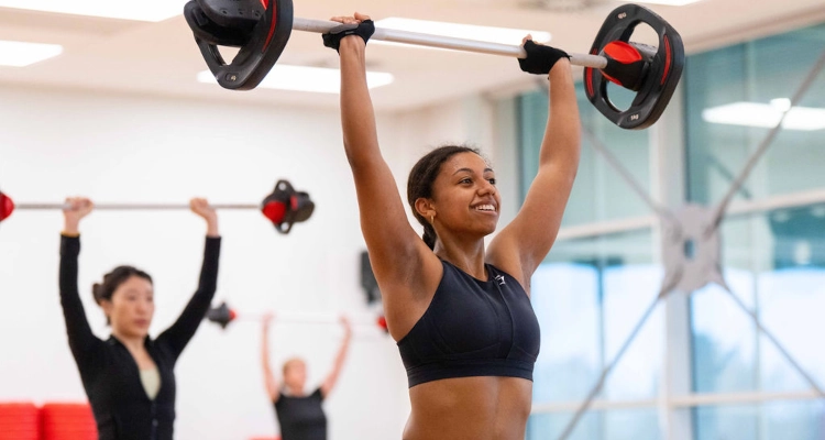 A person attending a HIIT session and raising a barbell above their head