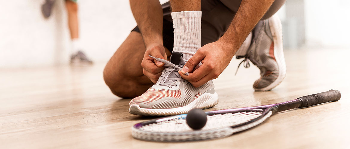 Man tying his shoe lace on a squash court