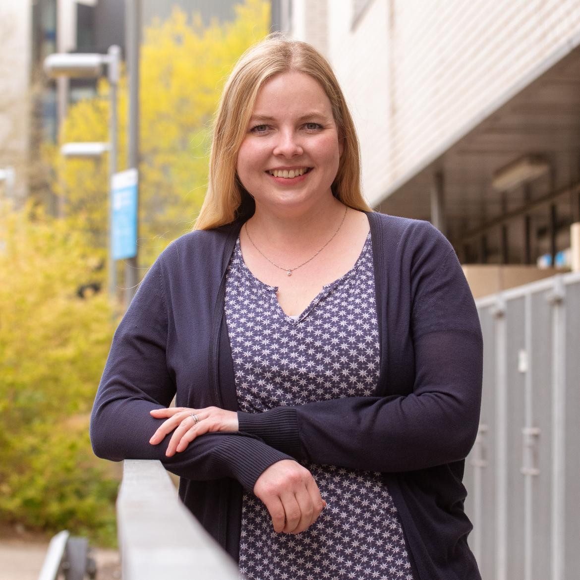 Image of a woman leaning against a curved fence, with a blurred background