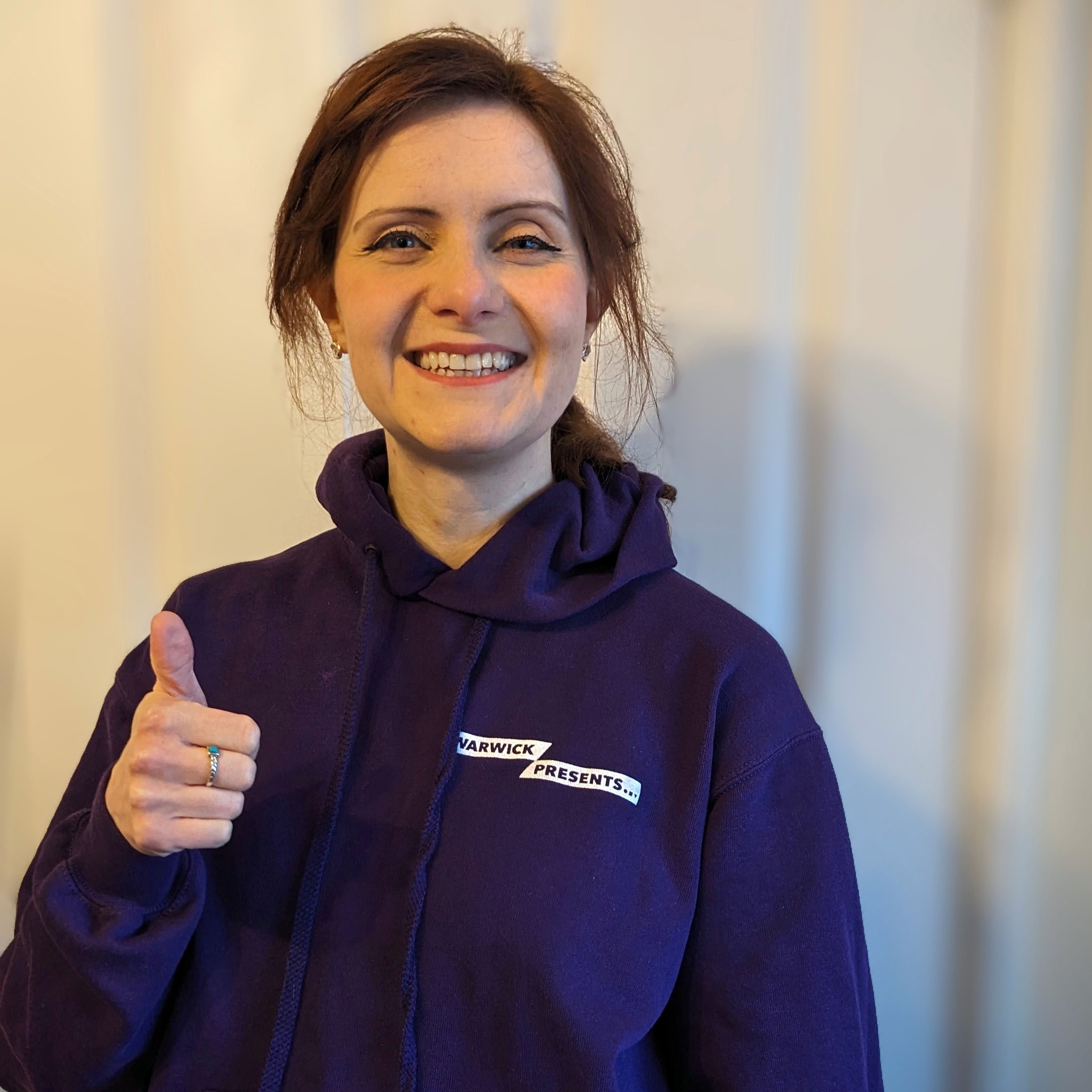 Image of a woman in a purple hoodie with her thumbs up on a white background.