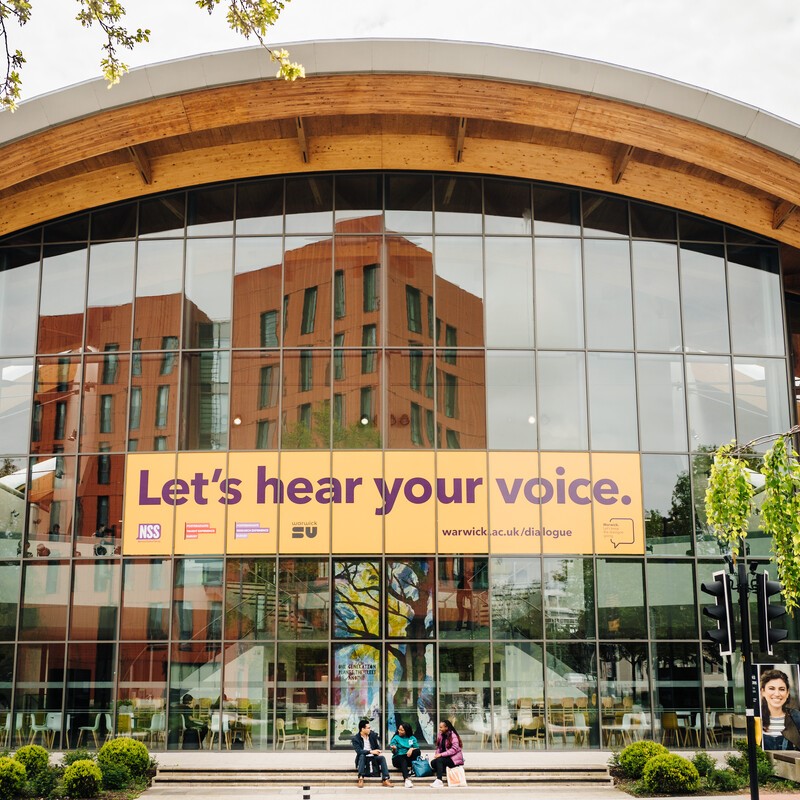 Image of the front of the Oculus building on Warwick Campus, with a 'Lets hear your voice' banner spread across several of the windows.