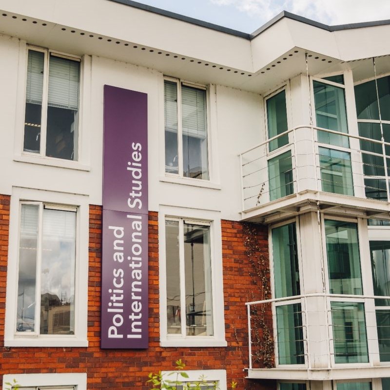 Image of a brick building with white cladding on the top half, a dark purple sign reads Politics and International Studies