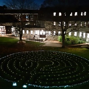 Image of a office building at night, with the windows lit up in the background and the focus on a series of lights on the grass in front of the building, these form a spiral pattern spinning out from a central point.