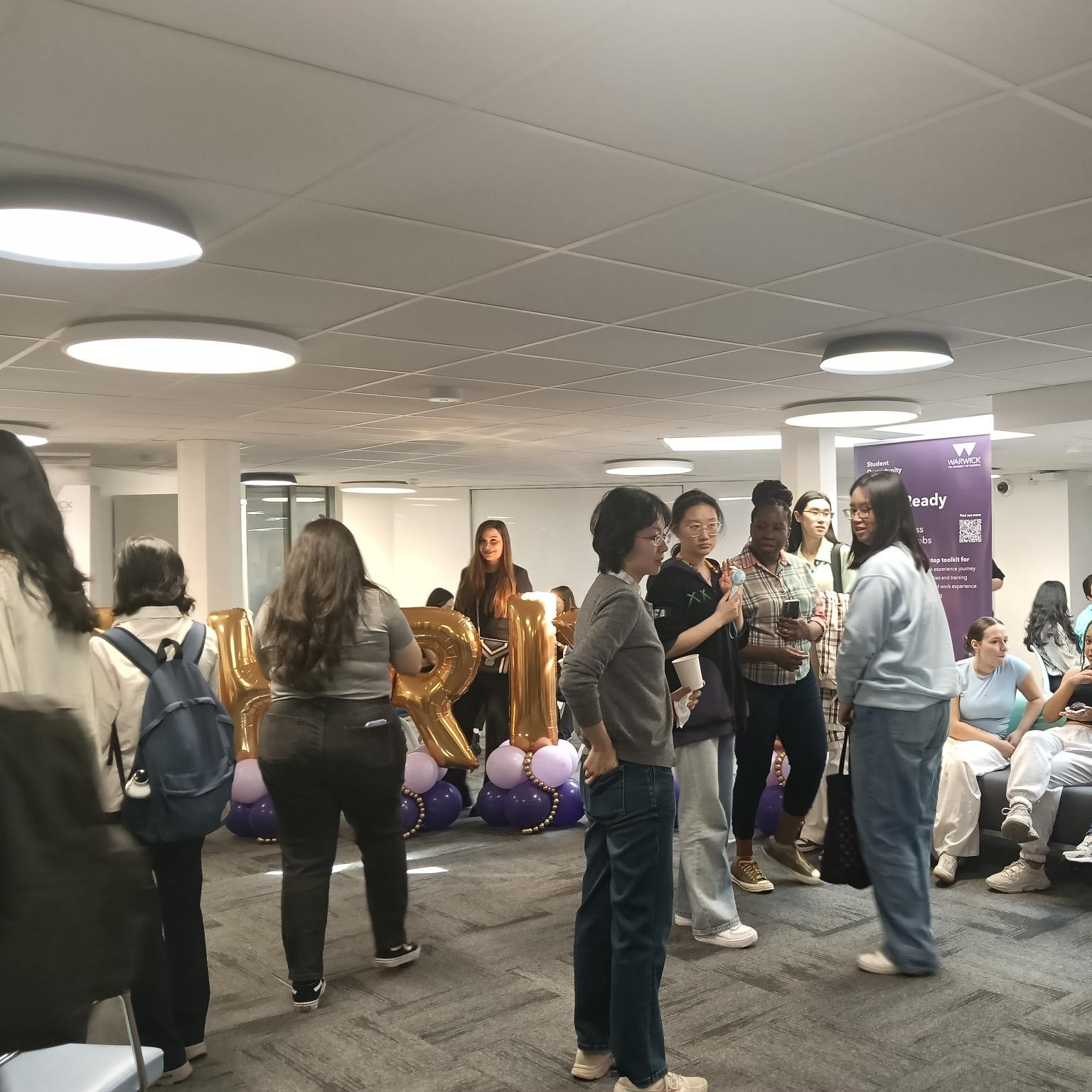 Image of a group of students milling about around a balloons that spell out THRIVE