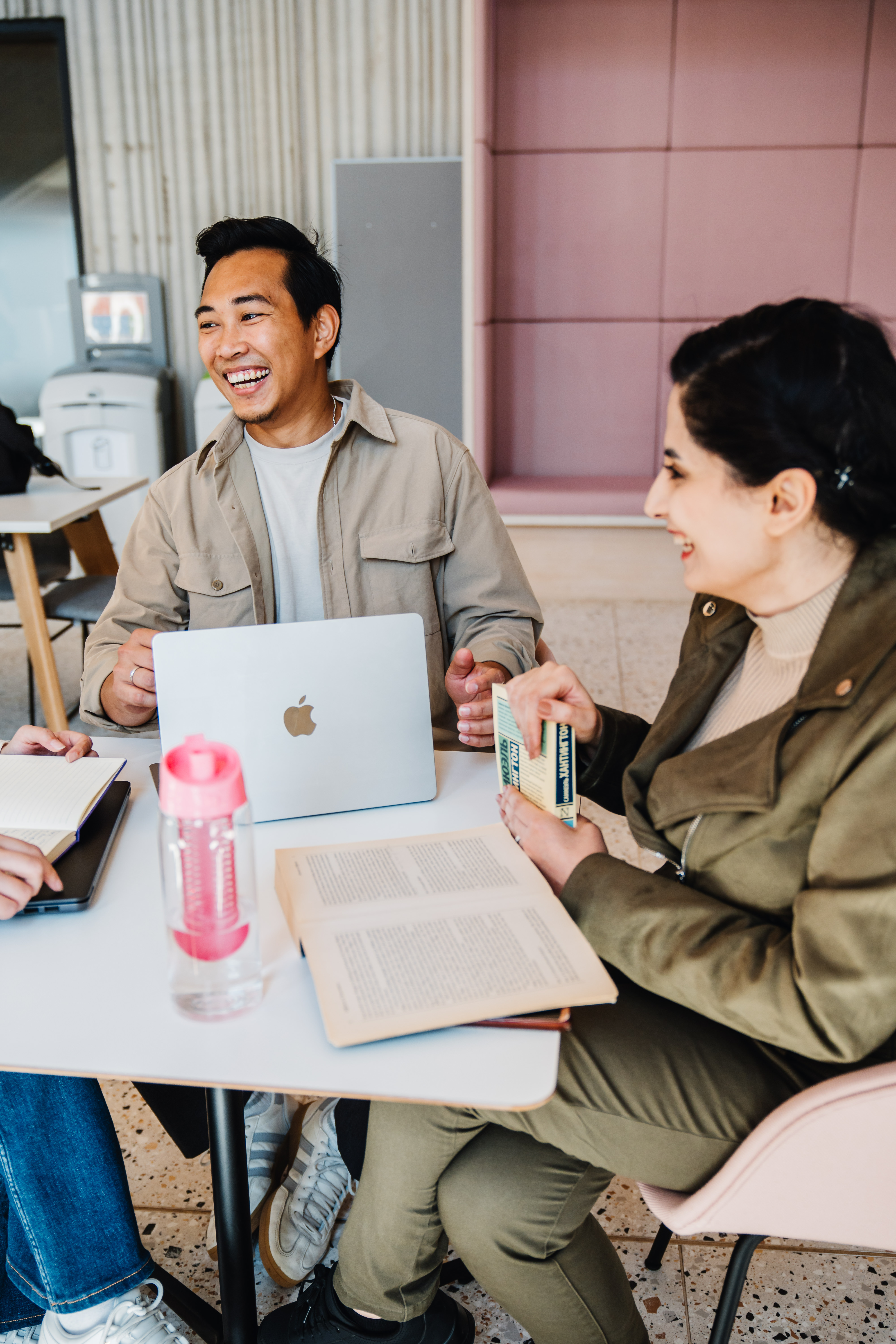 Two students laughing over a laptop and book