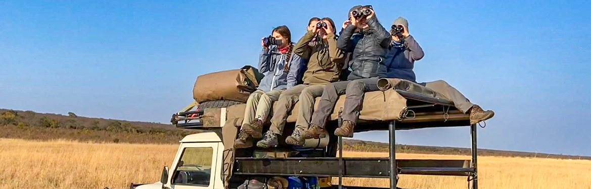 A group of people sitting on a land rover using binoculars