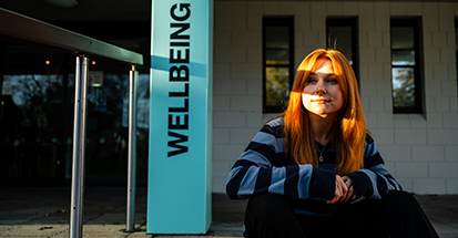 A student outside Senate House. Wellbeing is written on the pillar behind her.