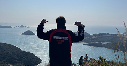 A student in a Team Warwick jacket flexing their arm muscles