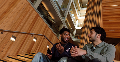 Two students, sat side by side, smiling at each other.