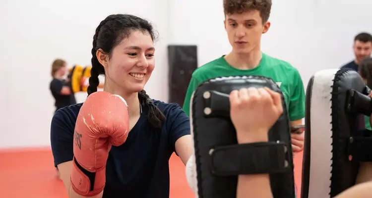 Person with gloves on punching training pads with instructor watching