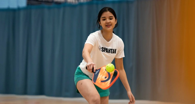 A student playing pickleball on a court within the Sports and Wellness Hub