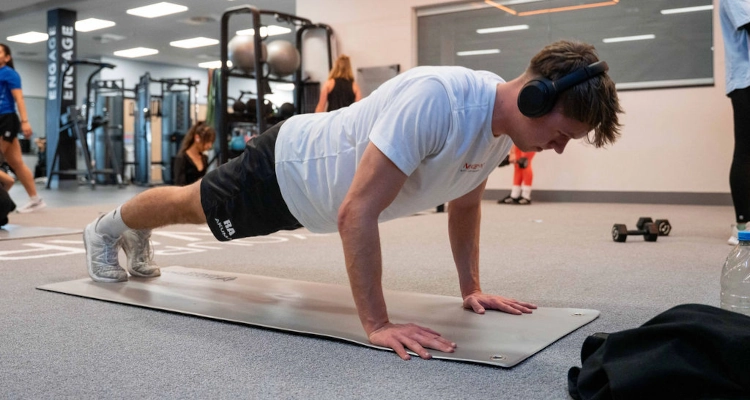 A person wearing black short and a white t-shirt doing pushups in the gym