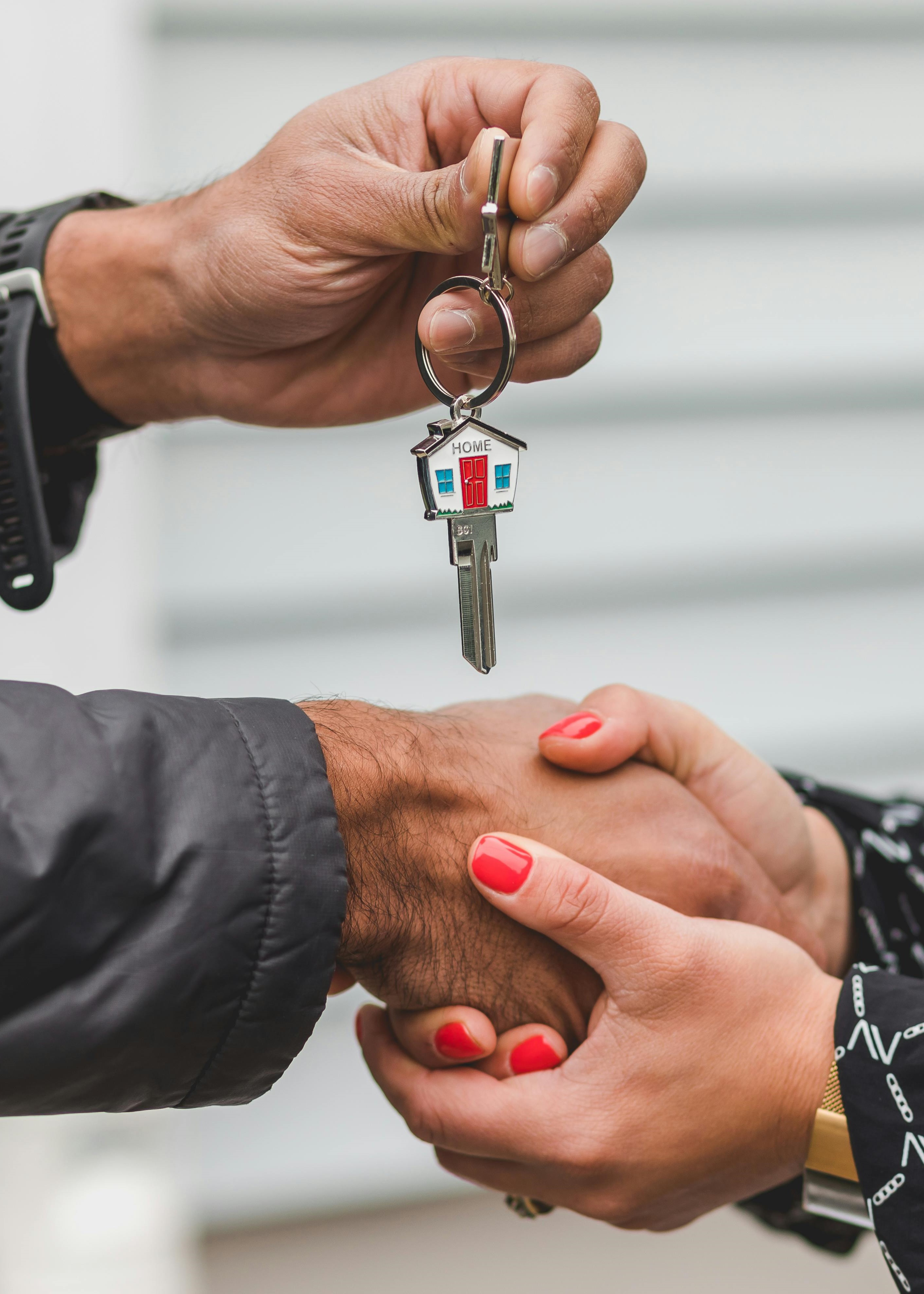 2 people shaking hands with a house key being held up between them.