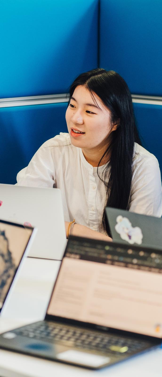 Image of a student in a blue meeting pod, with various laptops around them