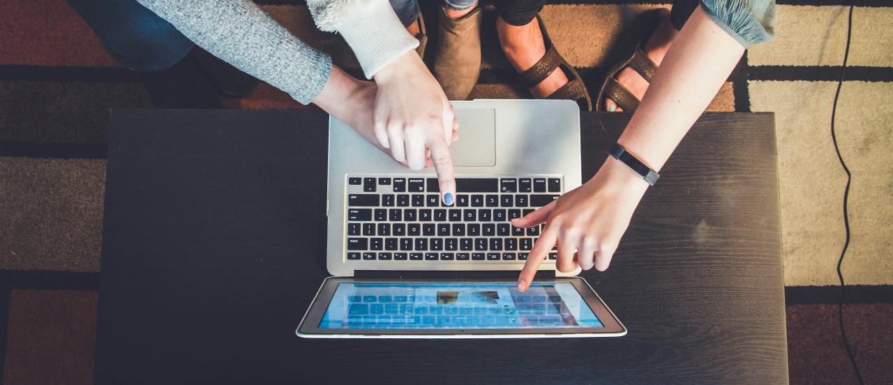 Different people pointing to a laptop computer screen on a low table, only their hands and feet are in the shot