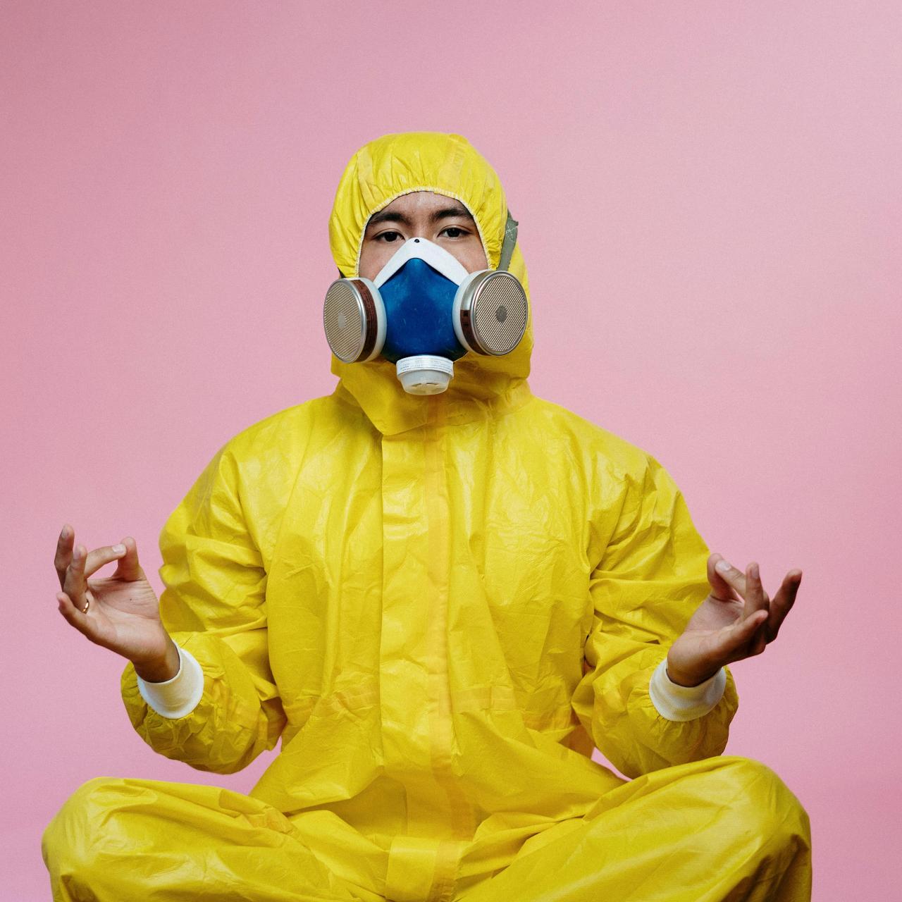 Image of a person in a yellow hazmat suit with a blue face mask on a pick background.