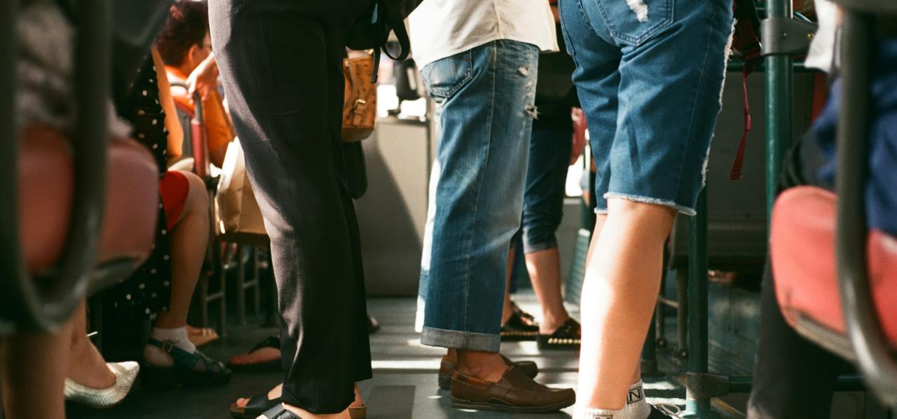 Image of a crowded passageway on a bus, showing the bottom half of a lot of peoples legs