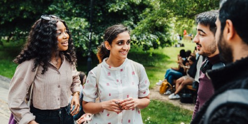 Image of 4 students talking, with a green area and some trees in the background