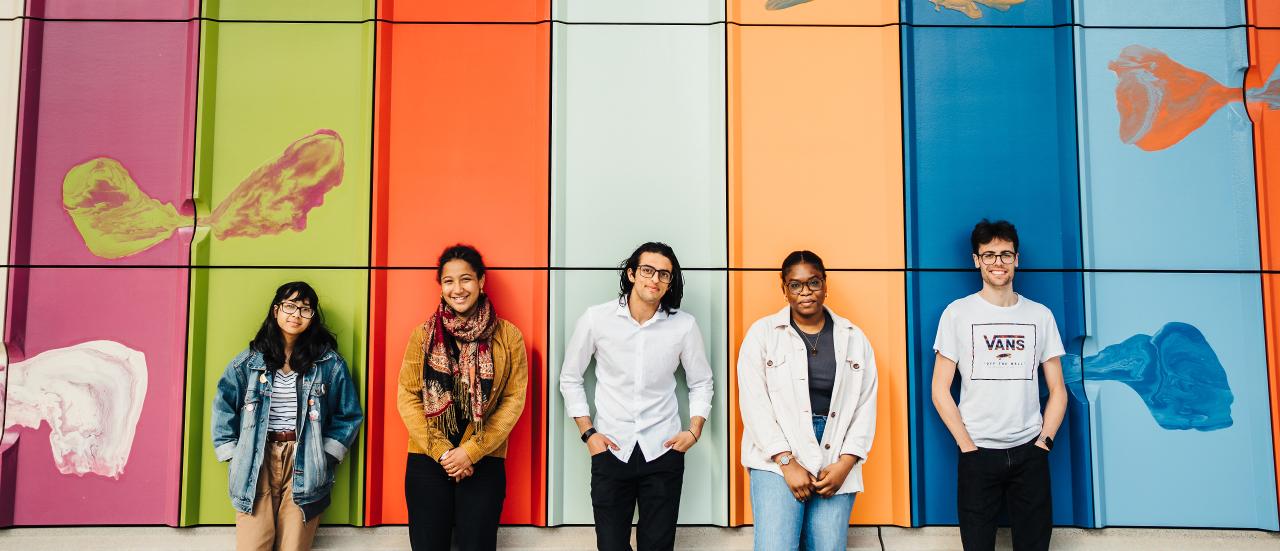 Image of a set of students standing in front of a building with different coloured panels behind them