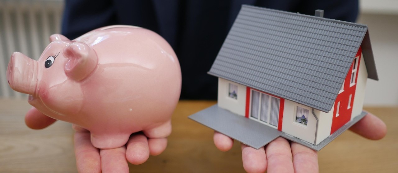 2 palms face up, one with a pink piggy bank and one with a small plastic house in it