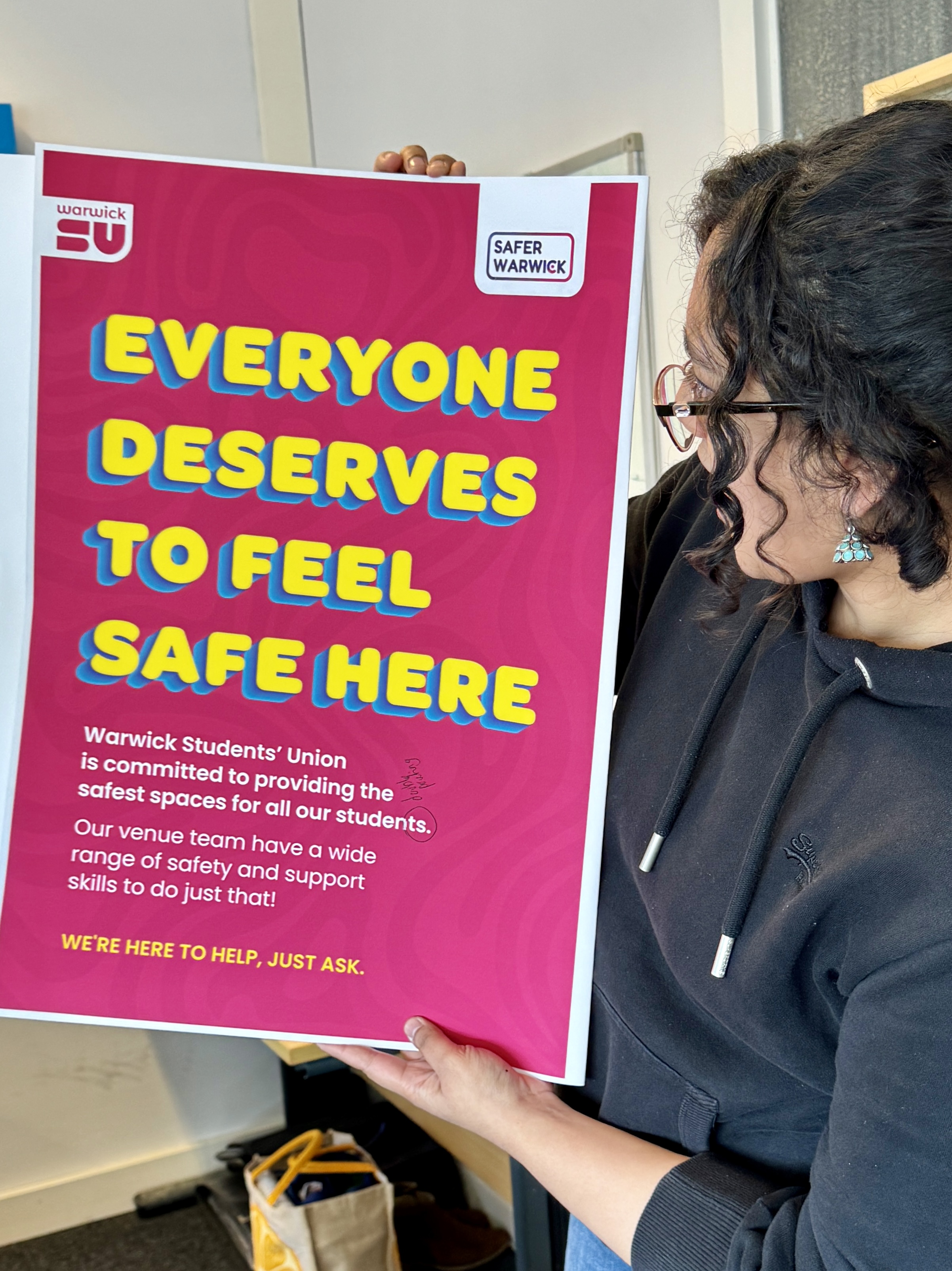 Enaya holding a poster that says 'everyone deserves to feel safe here'