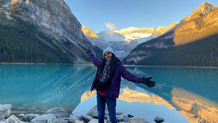 A student stands in front of a lake and mountains
