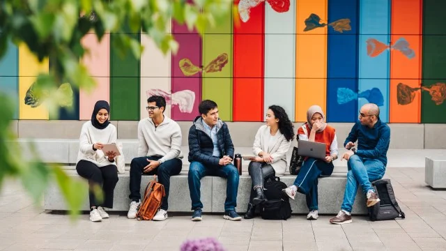 Six people are sat outside in front of a colourful background.