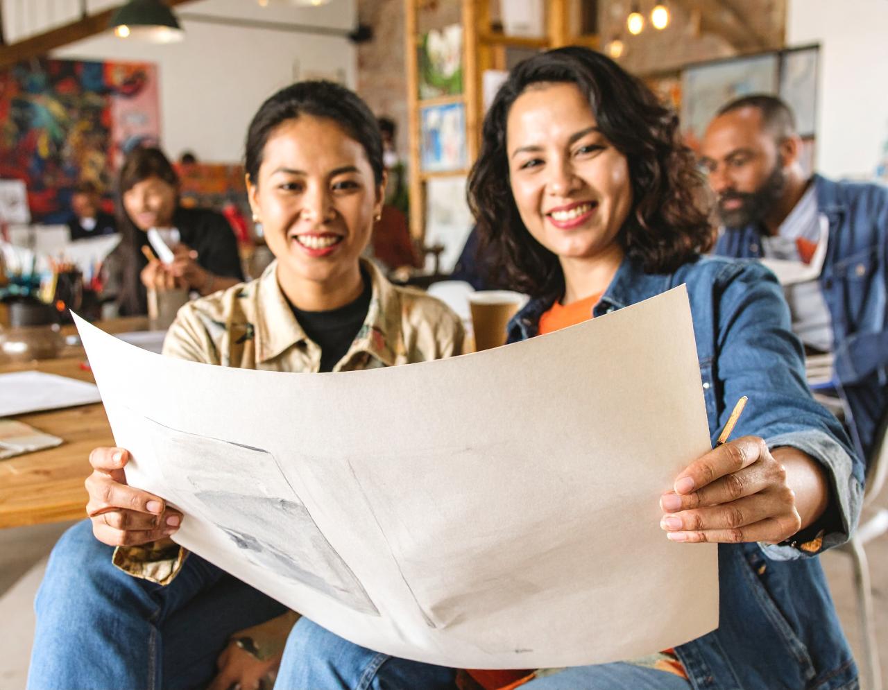 two students sitting next to each other, looking at a piece of paper that they are both holding up together. 