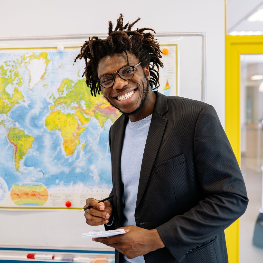 Man with paper and pen smiles with map behind
