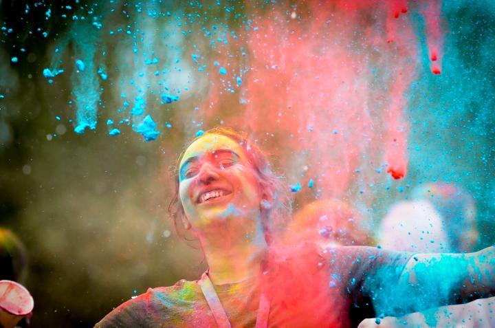 A student closes their eyes and stretches out their arms as colour powder rains from the sky.