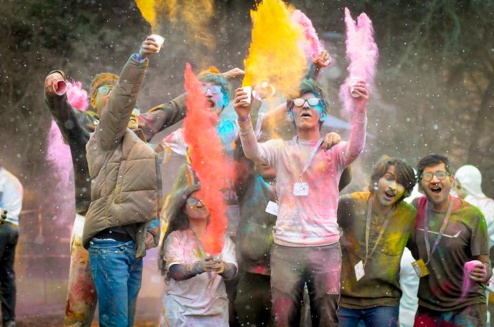 A group of students pose for the camera throwing cups of colour powder in the air.