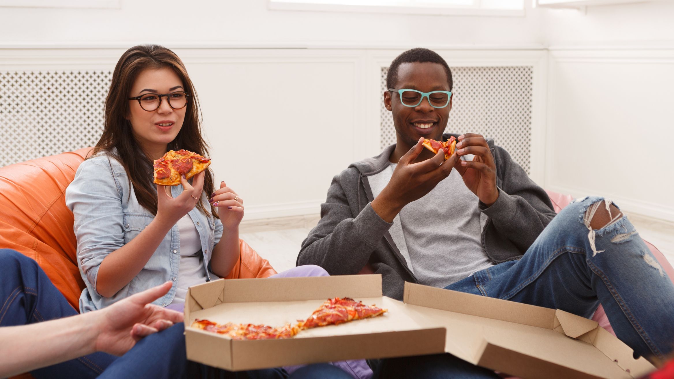 Two people sitting on beanbags in conversation and eating pizza