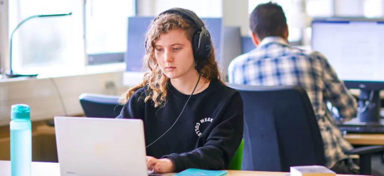 A student wearing headphones looks at a laptop screen