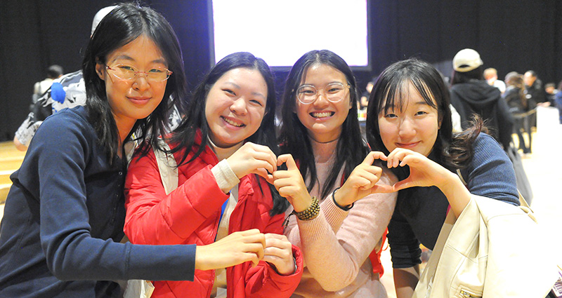 A group of students make hearts with their hands at the International Student Welcome