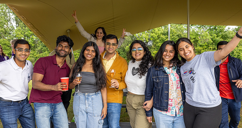 A group of students stand under a stretch tent and smile at the camera