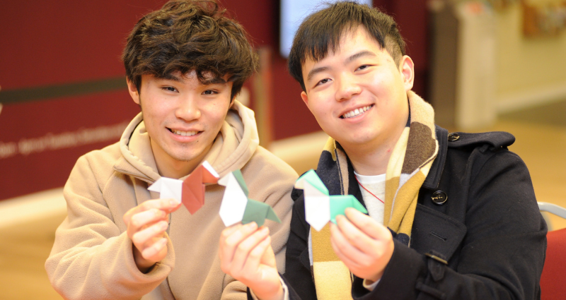 Two students smiling and holding up origami