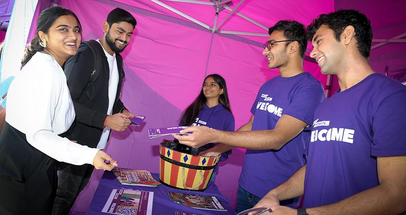 A group of students chat to welcome helpers in purple t-shirts inside a purple gazebo