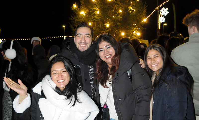 A group of students smile in front of the Chritsmas tree