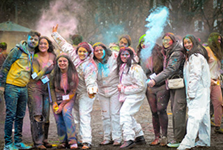 A group of students smiling, colour powder and snow surrounding them.