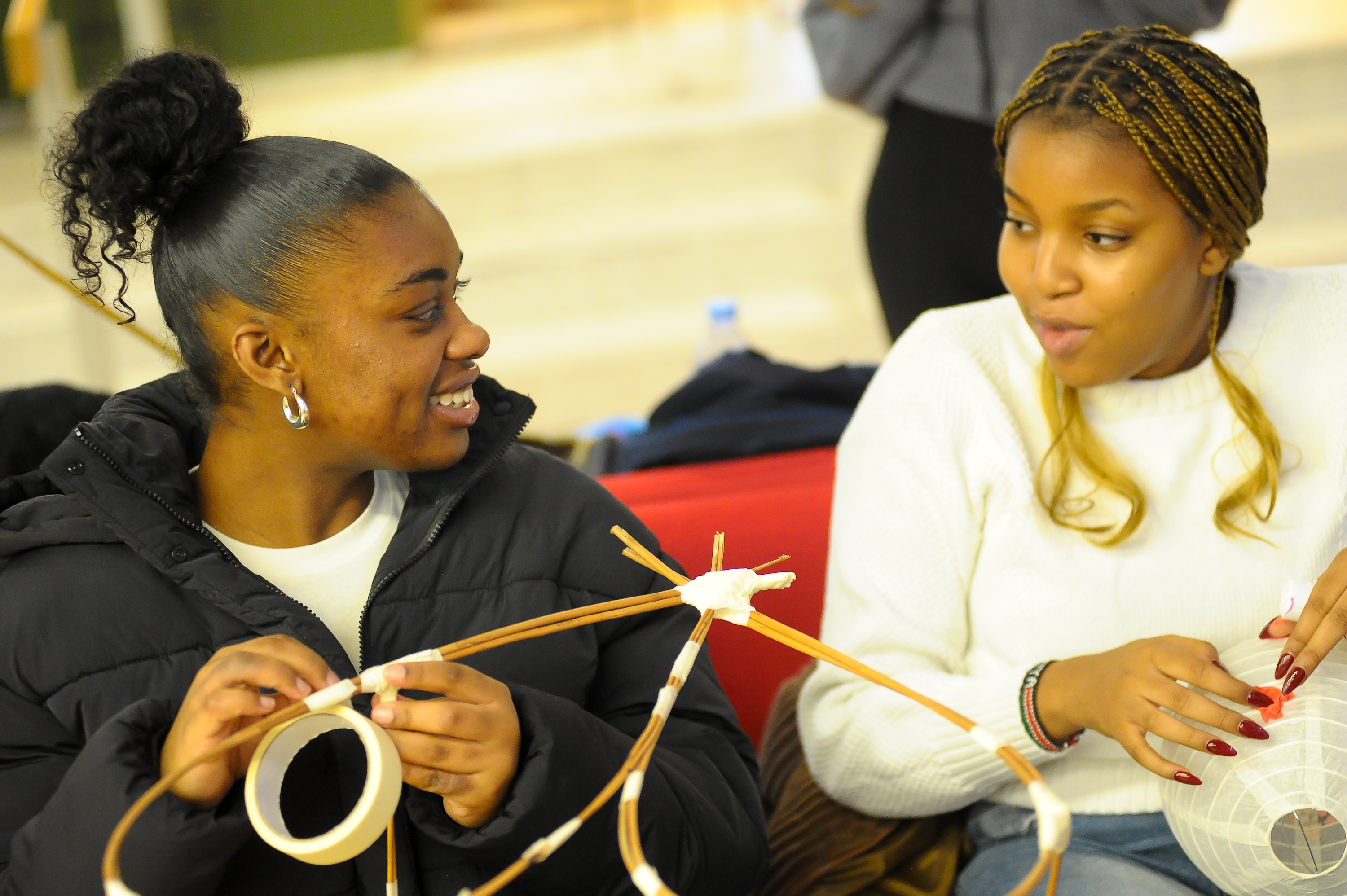 Two girls sit and talk whilst crafting lanterns out of Bamboo