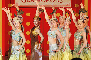 A group of dancers, wearing sparkly outfits and peacock feathers in their hair