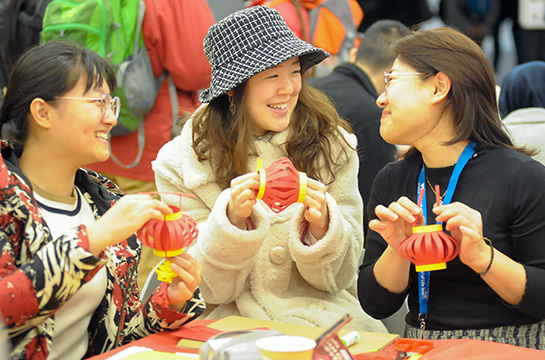 A group of three students laugh as they hold up paper lanterns they have crafted